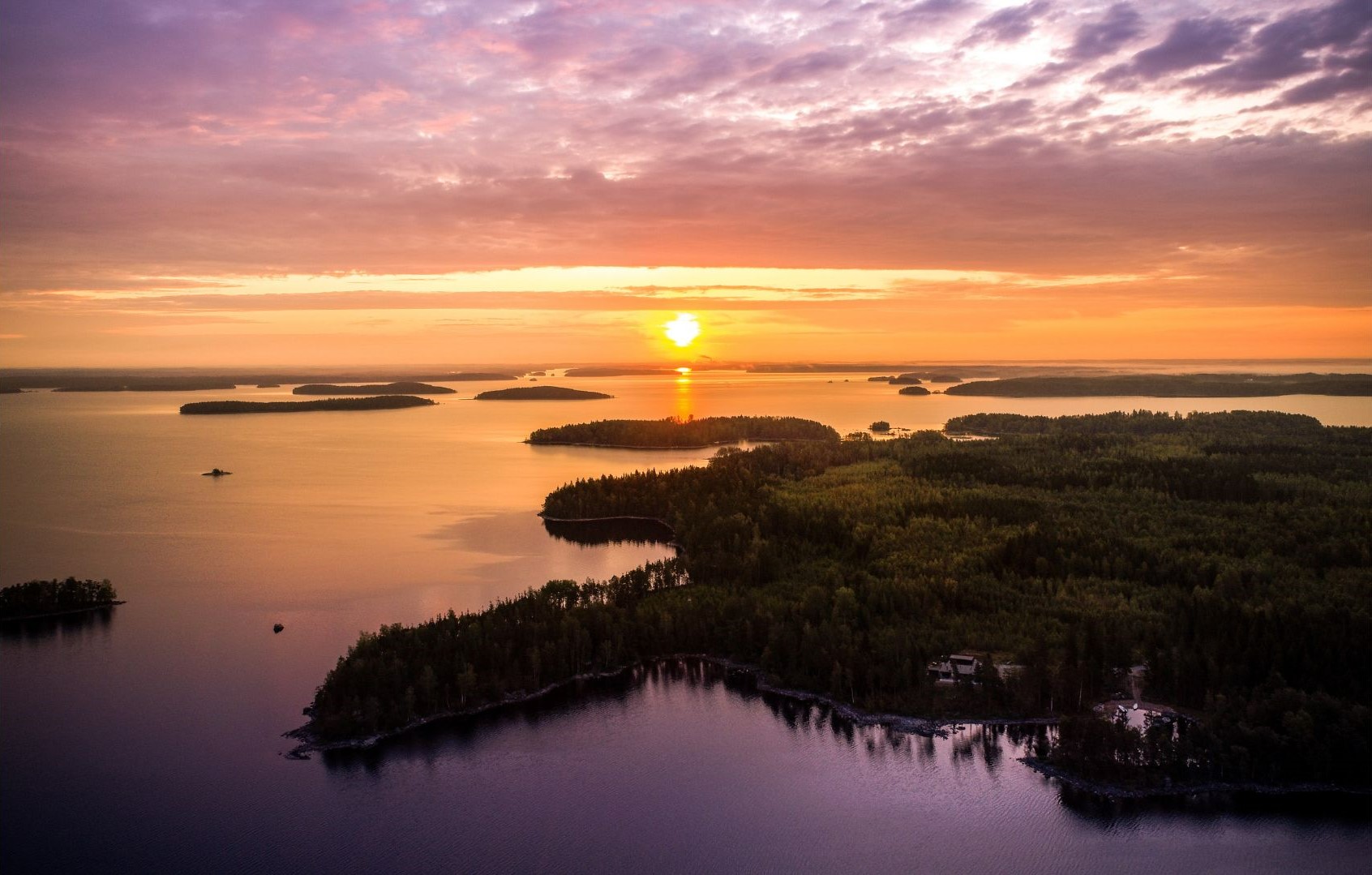 Saimaan vesistöä ja saaristoa. Kuvassa näkyy laskeva aurinko. Taivaan lilat sävyt heijastuvat veden pintaan.